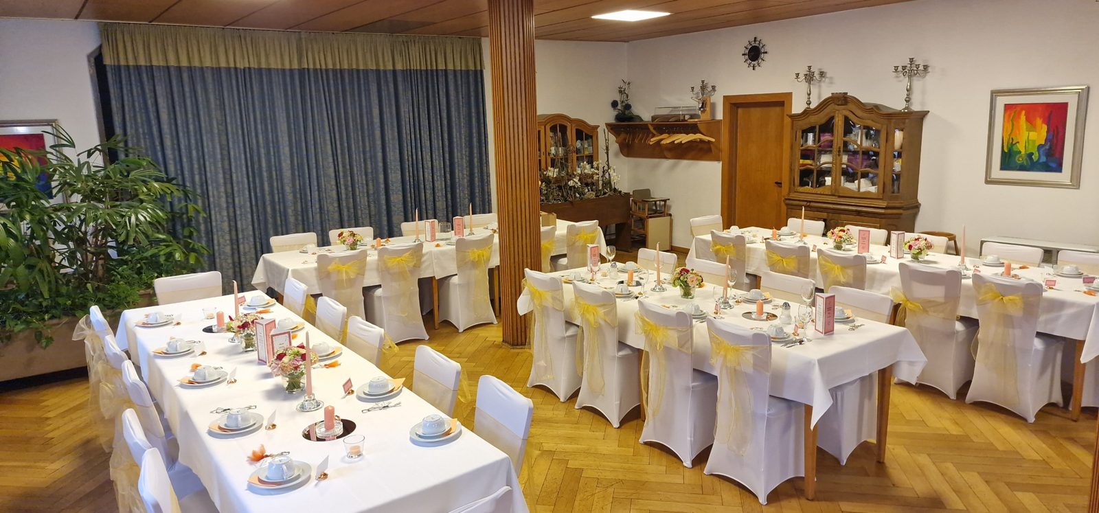 Festlich gedeckte Tische im Saal mit weißen Stuhlhussen, Schleifen und Blumenschmuck für eine Hochzeit oder Familienfeier