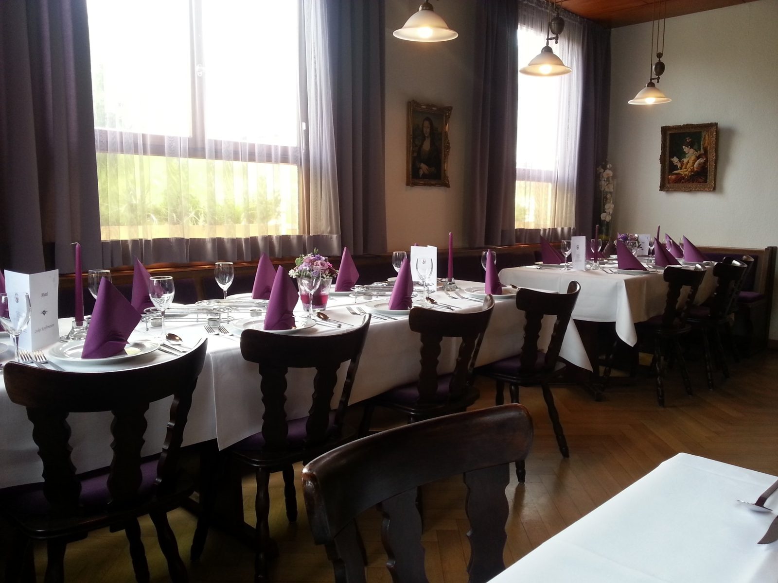Festlich gedeckte Tische mit weißen Tischdecken, lila Servietten und Blumenschmuck in der Gaststube des Hotels Zum Goldenen Hahnen